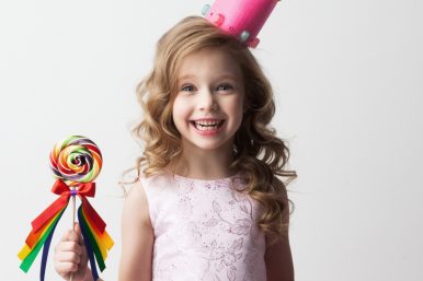 Beautiful little candy princess girl in crown holding big lollipop and smiling